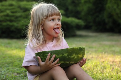 Photo of Cute little girl with half of juicy watermelon on green grass outdoors