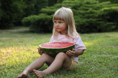 Photo of Cute little girl with half of juicy watermelon on green grass outdoors