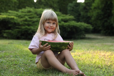 Photo of Cute little girl with half of juicy watermelon on green grass outdoors