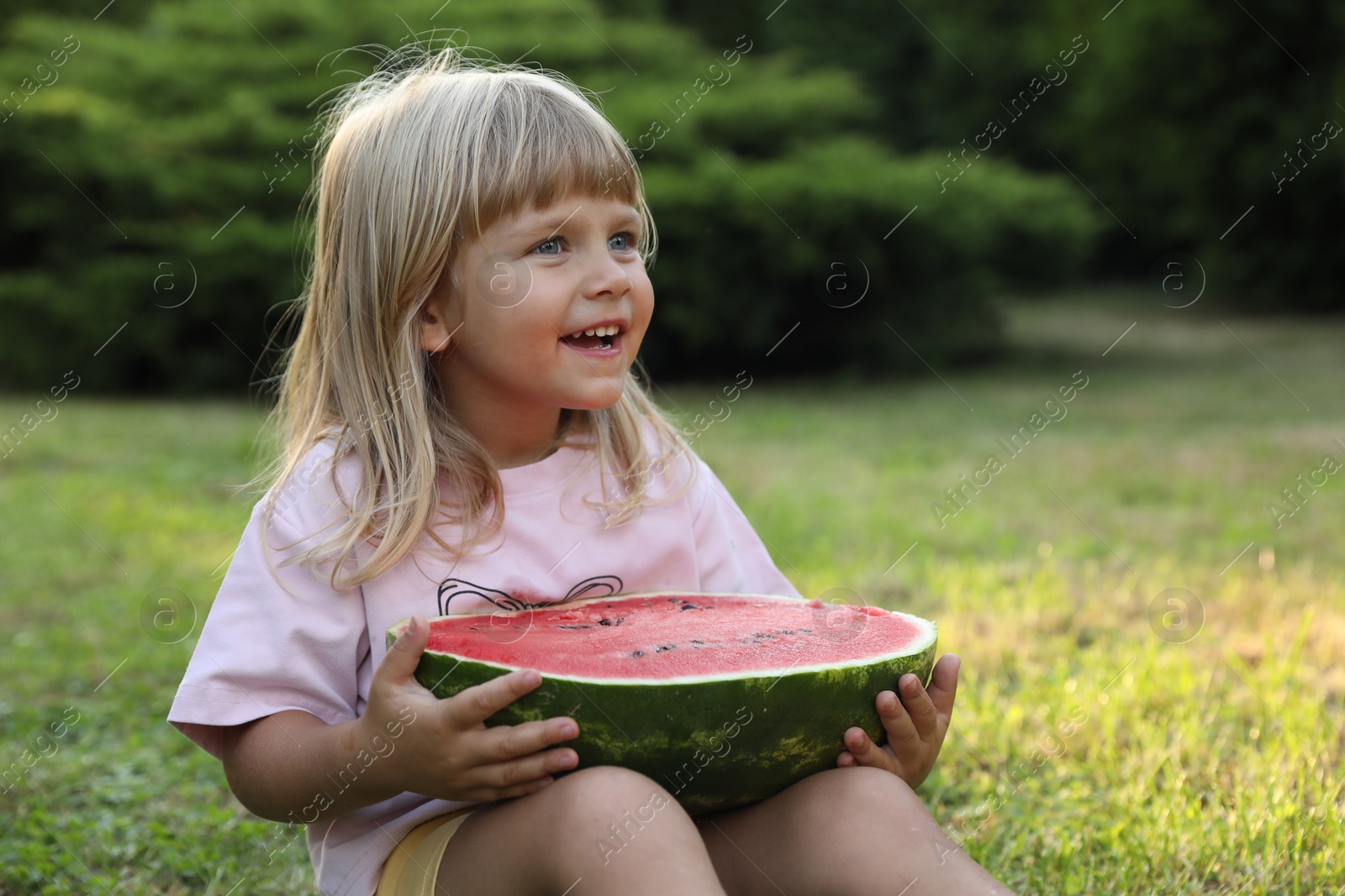 Photo of Cute little girl with half of juicy watermelon on green grass outdoors