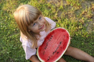 Cute little girl with half of juicy watermelon on green grass outdoors, above view