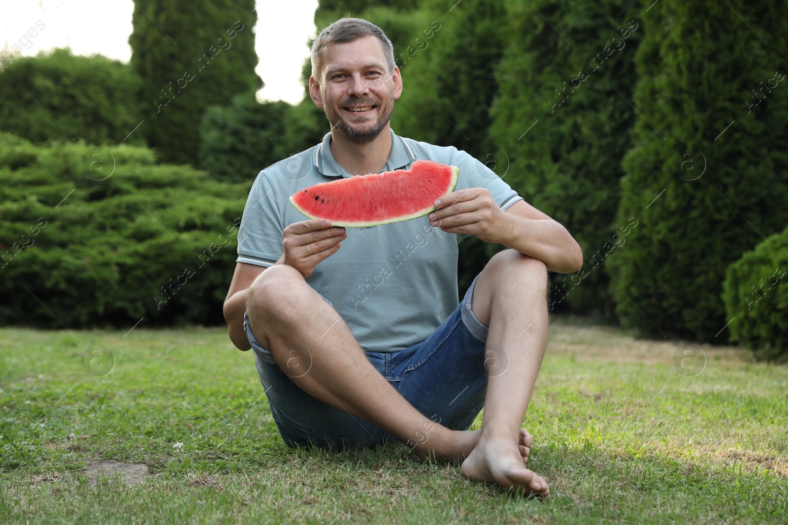 Photo of Happy man with slice of juicy watermelon outdoors