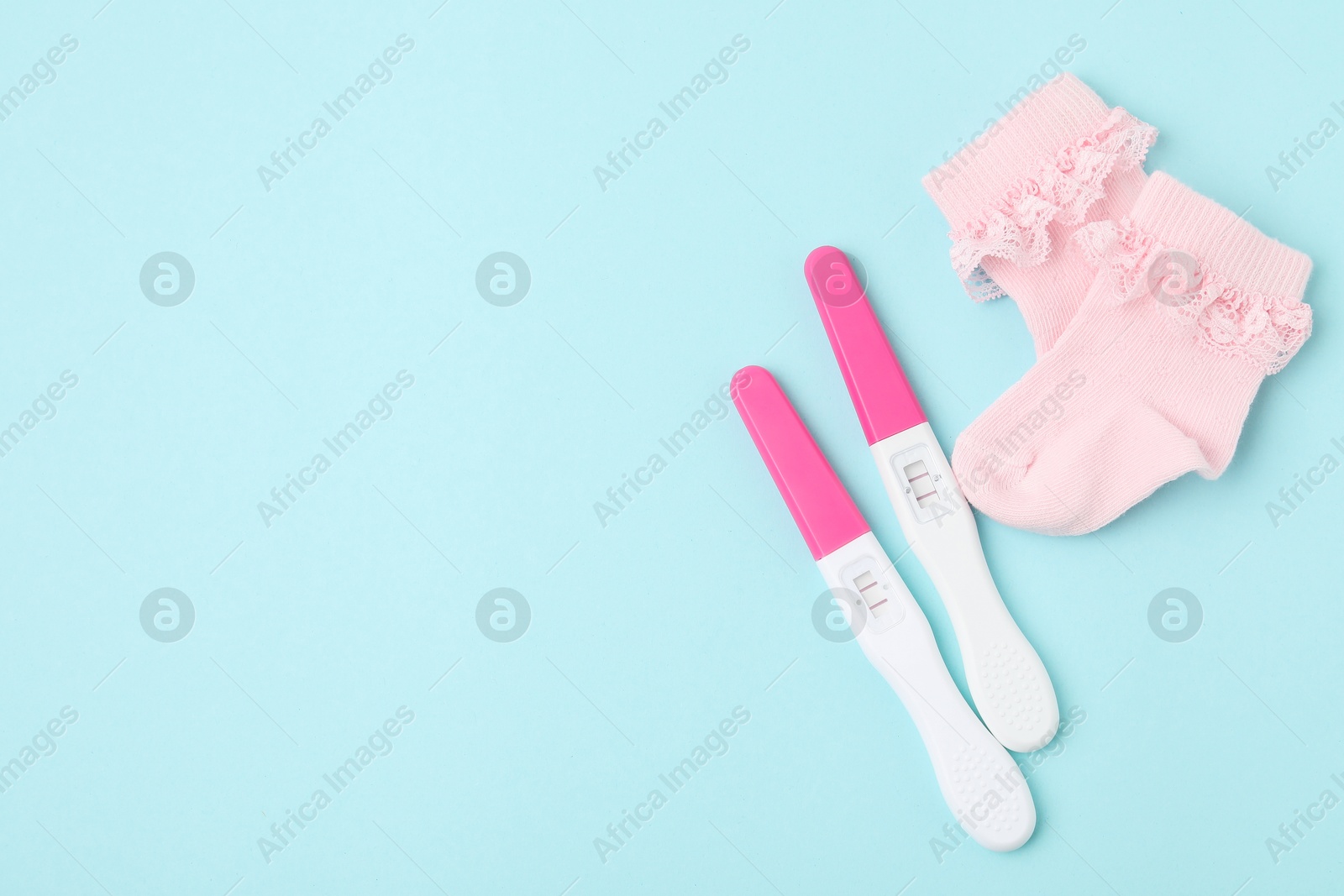 Photo of Pregnancy tests and pink socks on light blue background, top view. Space for text