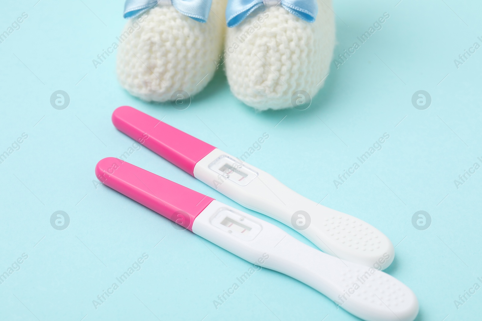 Photo of Pregnancy tests and knitted booties on light blue background, closeup