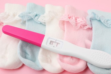 Photo of Pregnancy test and socks on pink background, closeup