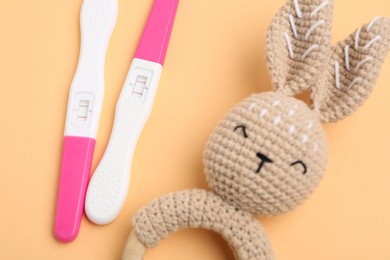 Photo of Pregnancy tests and baby rattle on pale orange background, closeup