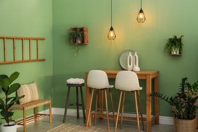 Photo of Bar stools, table and plants in room. Stylish interior design