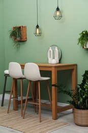 Photo of Bar stools, table and plants in room. Stylish interior design