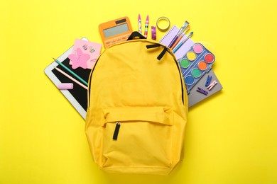 Photo of School backpack and stationery on yellow background, flat lay