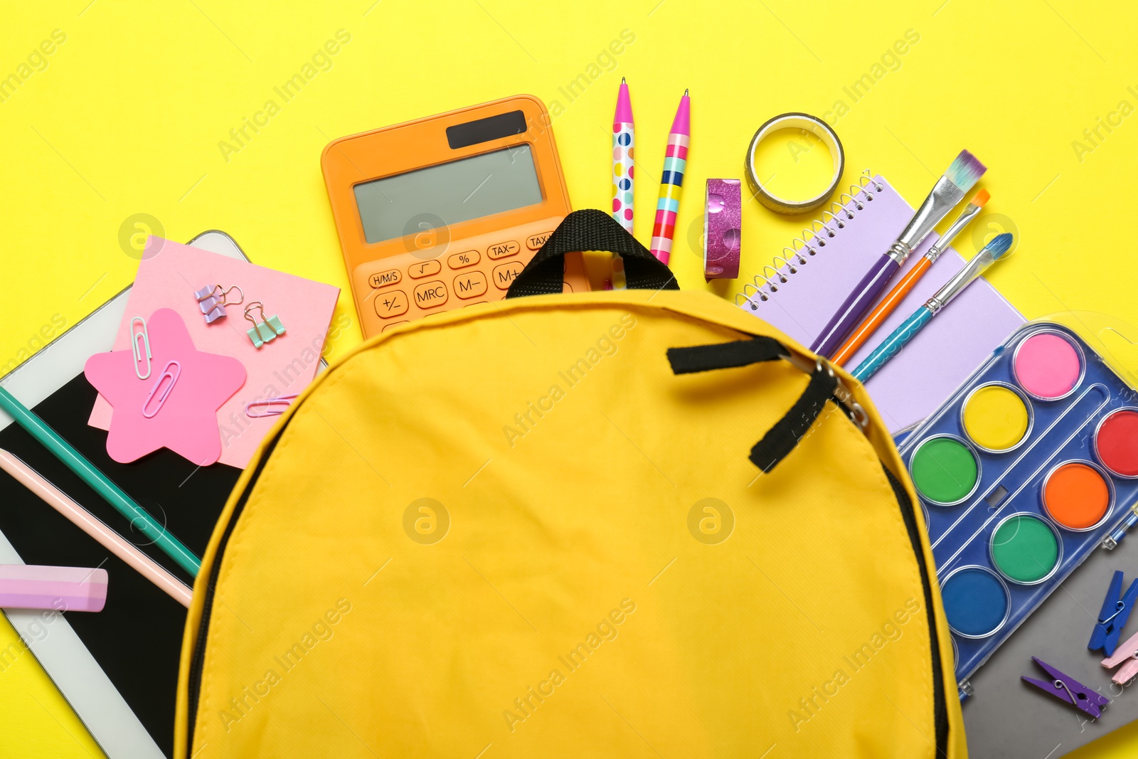 Photo of School backpack and stationery on yellow background, flat lay