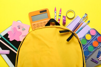 Photo of School backpack and stationery on yellow background, flat lay