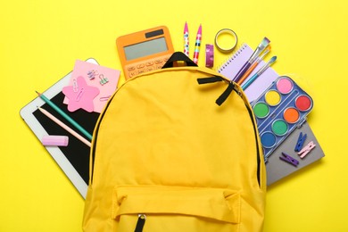 Photo of School backpack and stationery on yellow background, flat lay