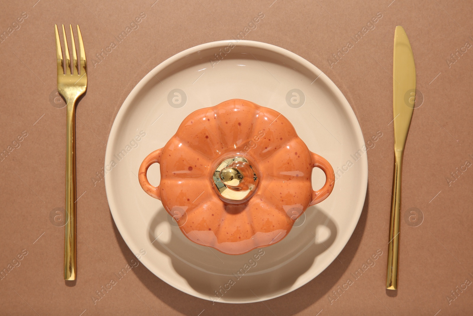 Photo of Beautiful table setting with cutlery and pumpkin shaped pot on brown background, flat lay