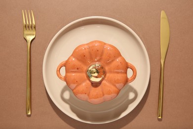 Beautiful table setting with cutlery and pumpkin shaped pot on brown background, flat lay