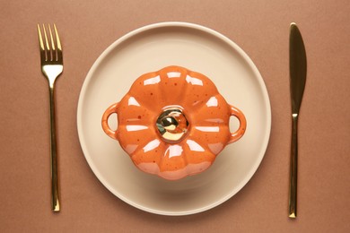 Beautiful table setting with cutlery and pumpkin shaped pot on brown background, flat lay