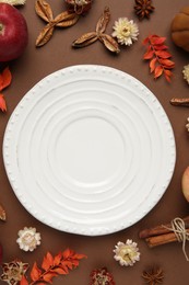 Stylish table setting. Plate and autumn decor on brown background, flat lay