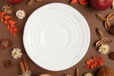 Stylish table setting. Plate and autumn decor on brown background, flat lay