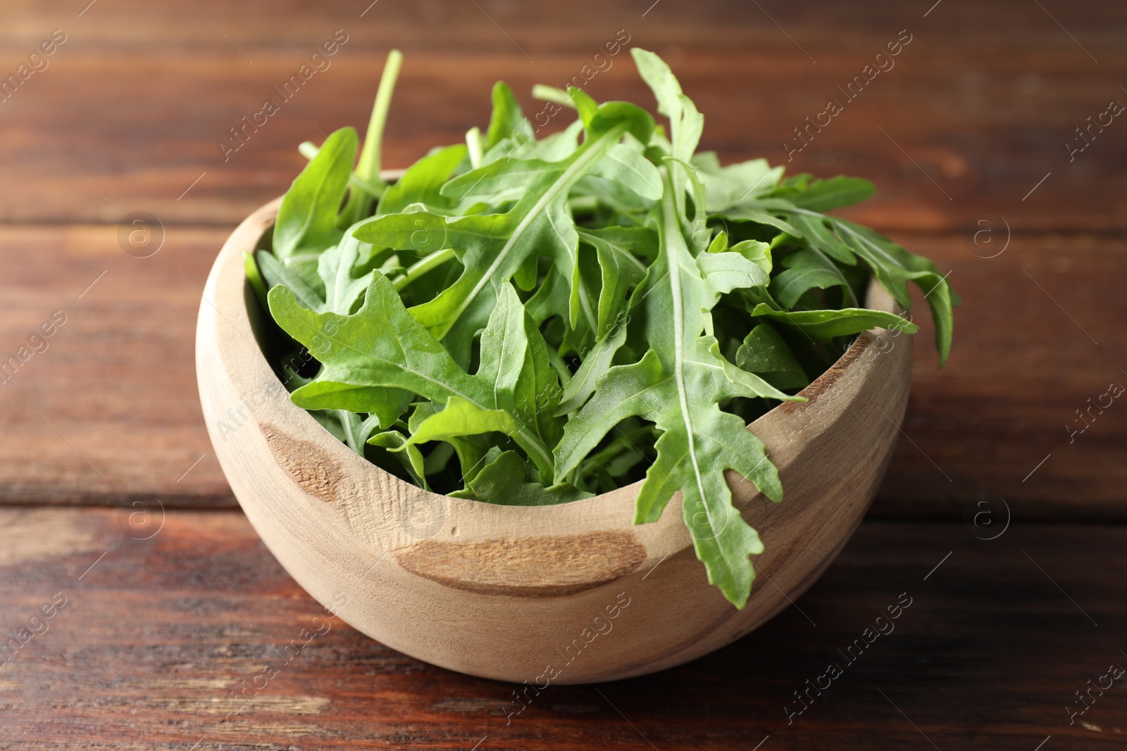 Photo of Fresh green arugula leaves in bowl on wooden table, closeup