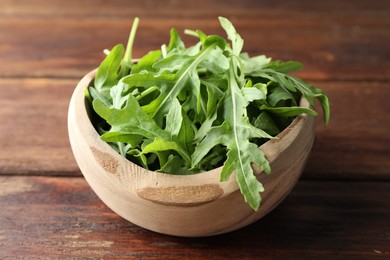 Photo of Fresh green arugula leaves in bowl on wooden table, closeup