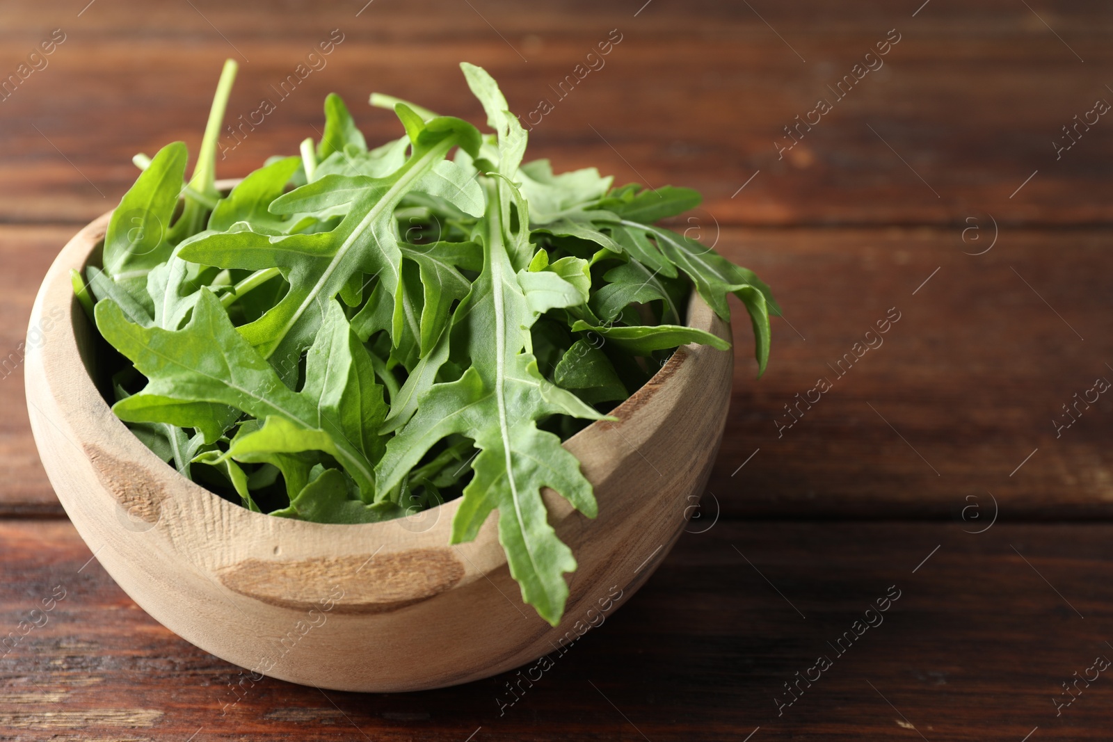 Photo of Fresh green arugula leaves in bowl on wooden table, closeup