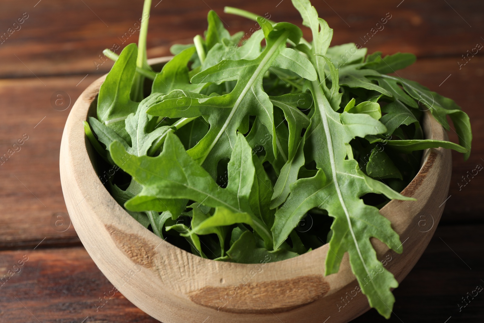 Photo of Fresh green arugula leaves in bowl on wooden table, closeup