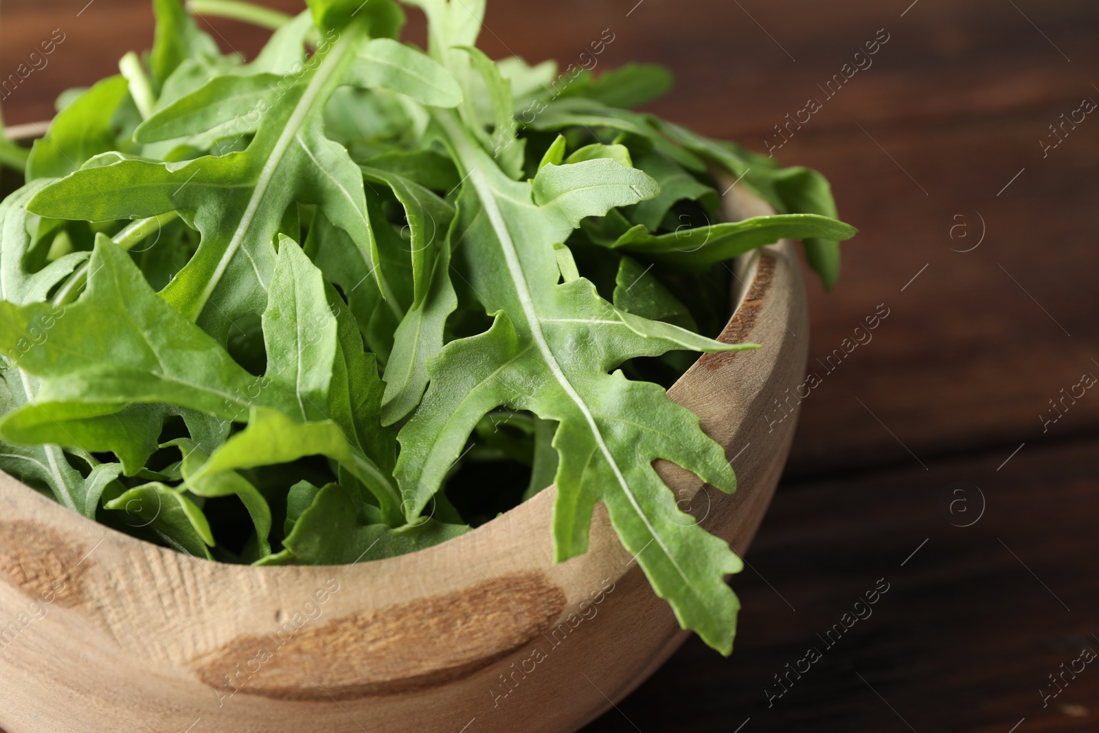 Photo of Fresh green arugula leaves in bowl on table, closeup