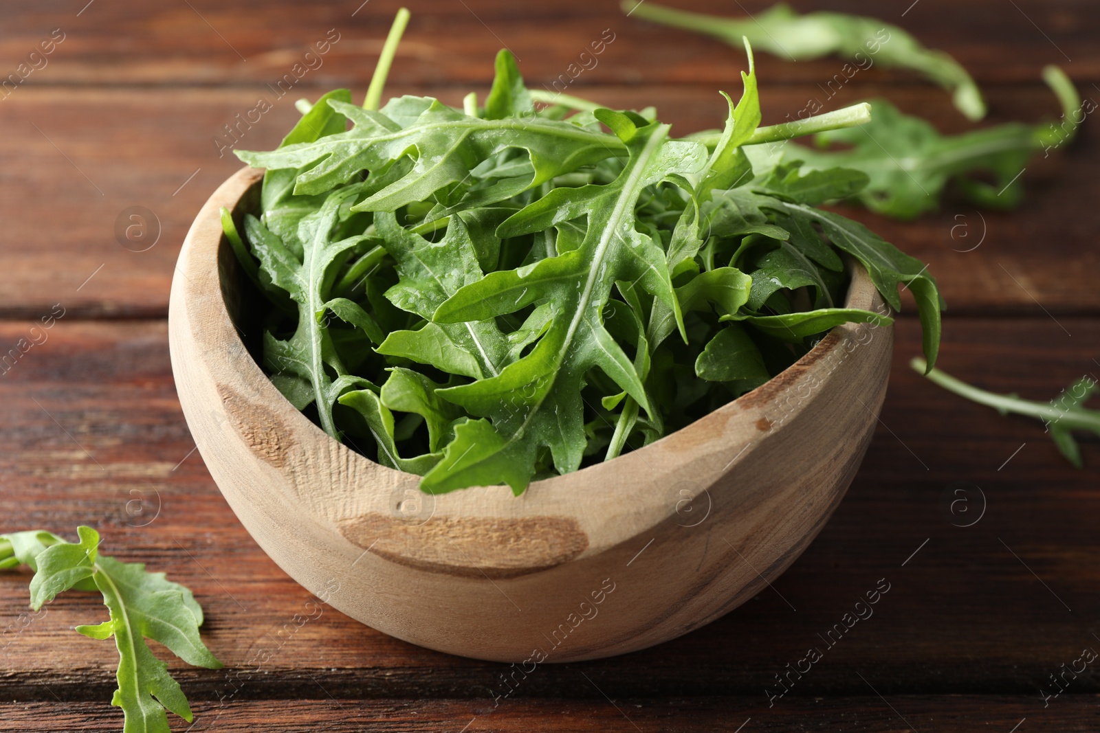 Photo of Fresh green arugula leaves in bowl on wooden table, closeup