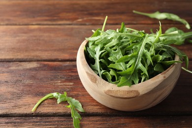 Photo of Fresh green arugula leaves in bowl on wooden table, closeup