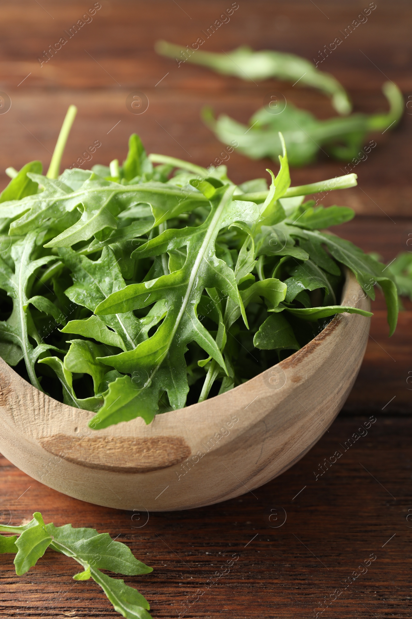 Photo of Fresh green arugula leaves in bowl on wooden table, closeup