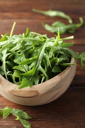 Photo of Fresh green arugula leaves in bowl on wooden table, closeup