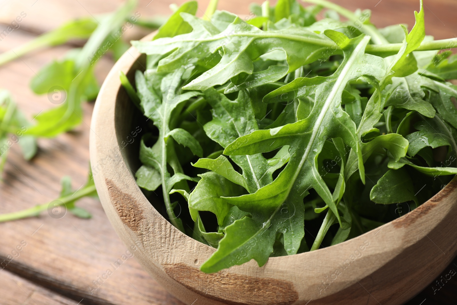 Photo of Fresh green arugula leaves in bowl on wooden table, closeup