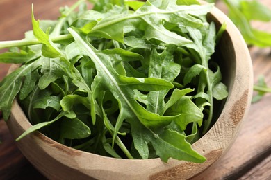 Photo of Fresh green arugula leaves in bowl on wooden table, closeup