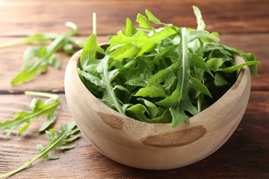 Photo of Fresh green arugula leaves in bowl on wooden table, closeup