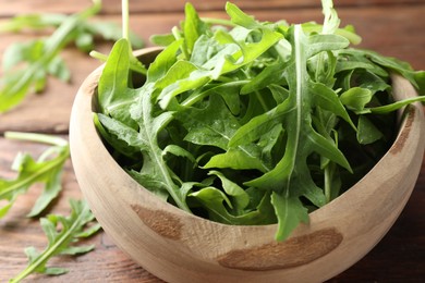 Photo of Fresh green arugula leaves in bowl on wooden table, closeup