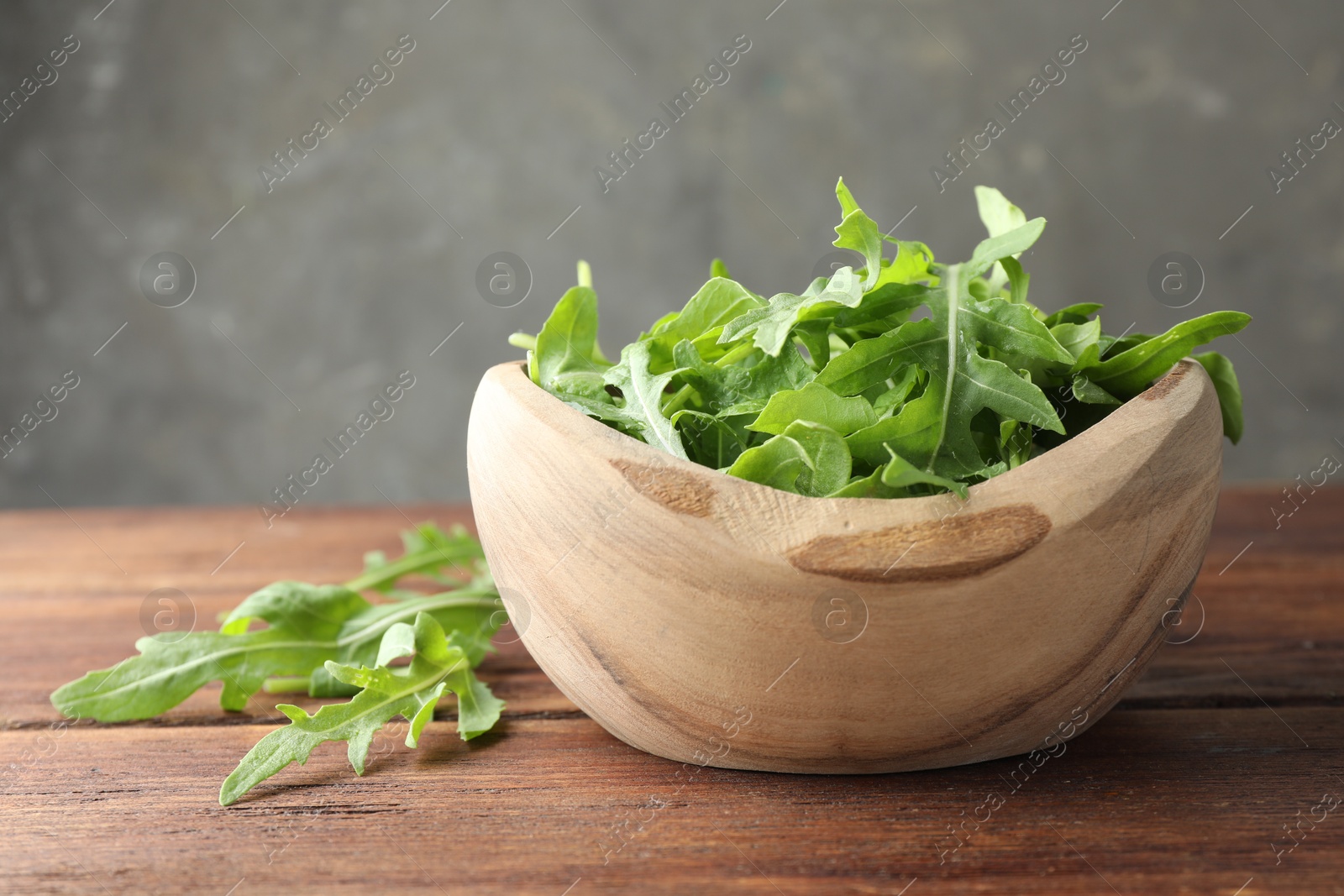 Photo of Fresh green arugula leaves in bowl on wooden table, closeup