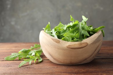 Photo of Fresh green arugula leaves in bowl on wooden table, closeup