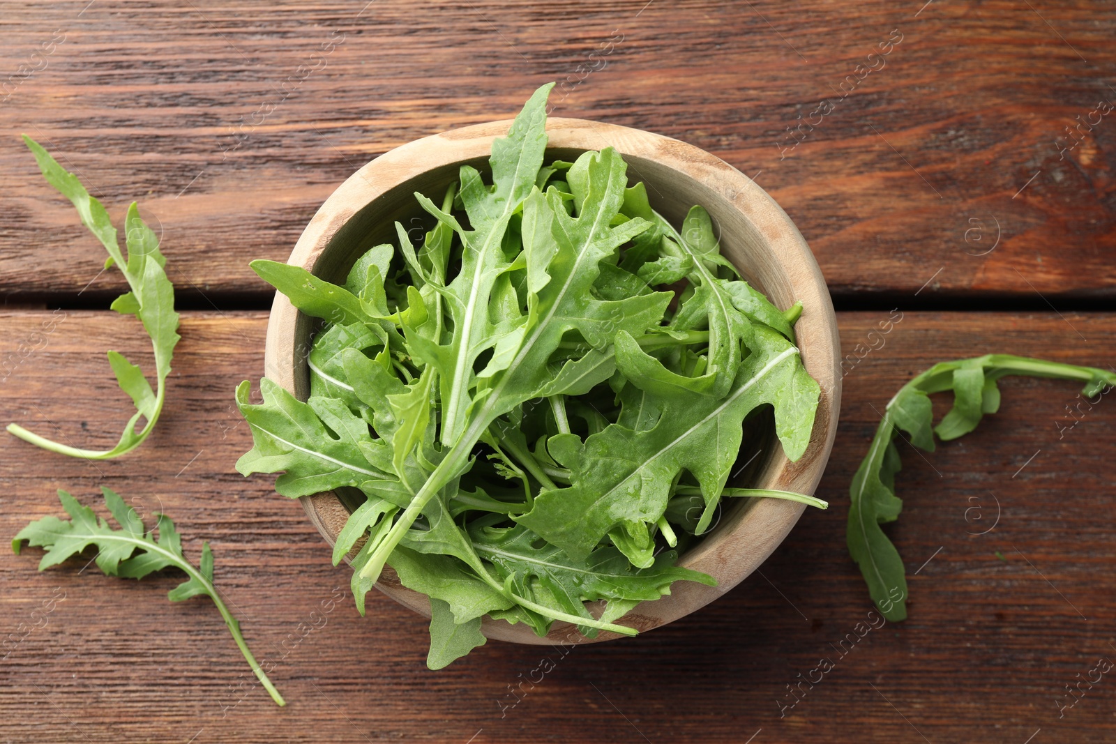 Photo of Fresh green arugula leaves in bowl on wooden table, top view