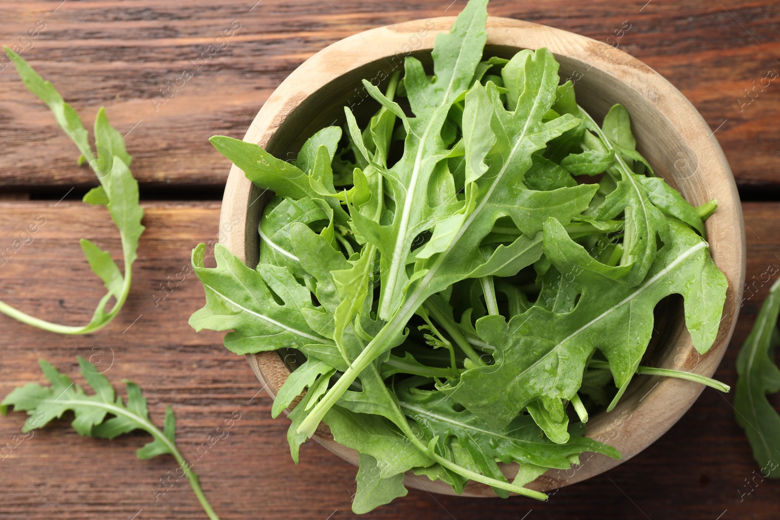 Photo of Fresh green arugula leaves in bowl on wooden table, top view