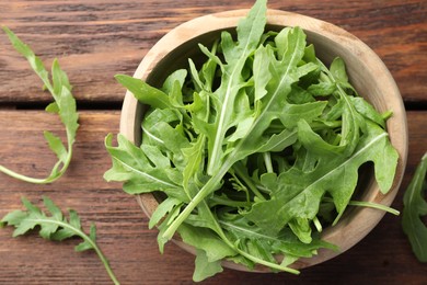 Photo of Fresh green arugula leaves in bowl on wooden table, top view