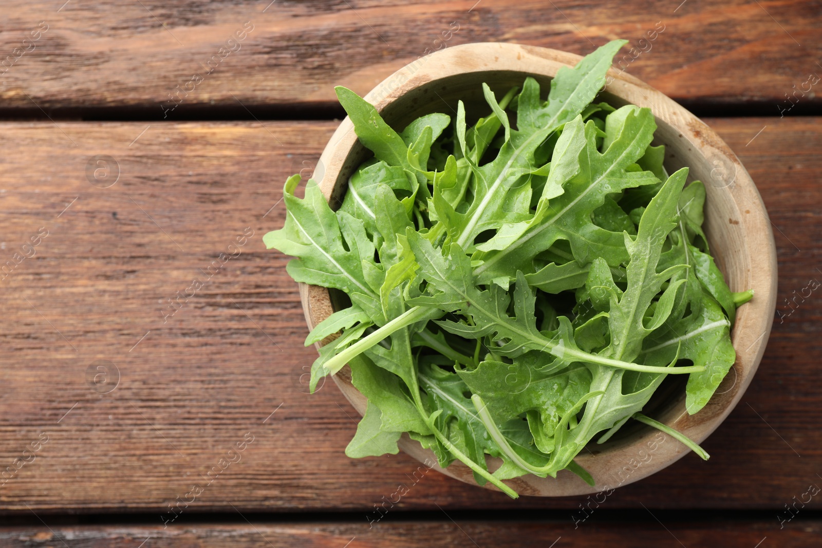 Photo of Fresh green arugula leaves in bowl on wooden table, top view. Space for text