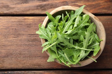 Photo of Fresh green arugula leaves in bowl on wooden table, top view. Space for text