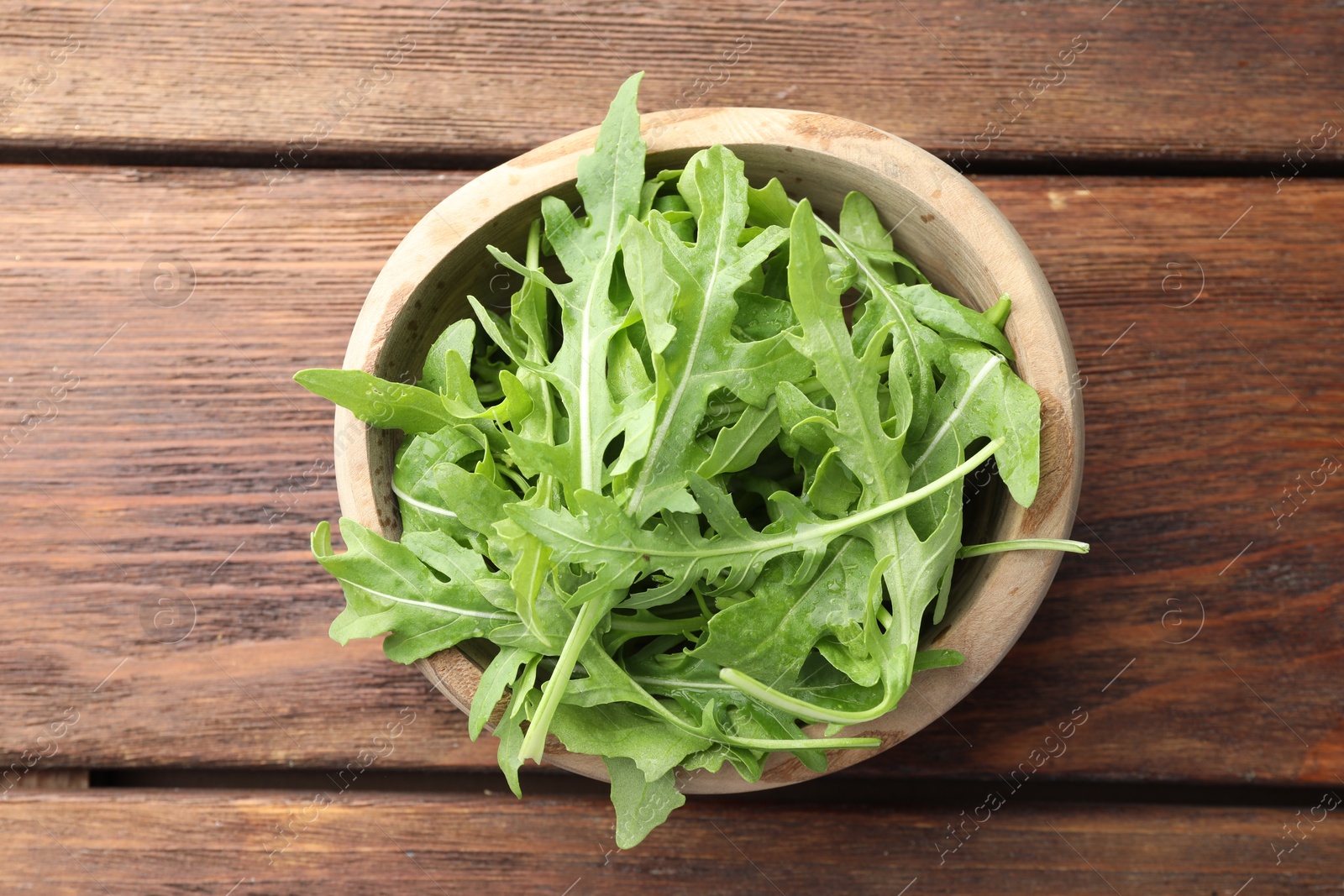 Photo of Fresh green arugula leaves in bowl on wooden table, top view