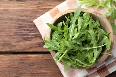 Photo of Fresh green arugula leaves in bowl on wooden table, top view. Space for text