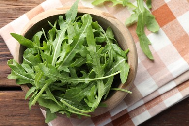 Photo of Fresh green arugula leaves in bowl on wooden table, top view