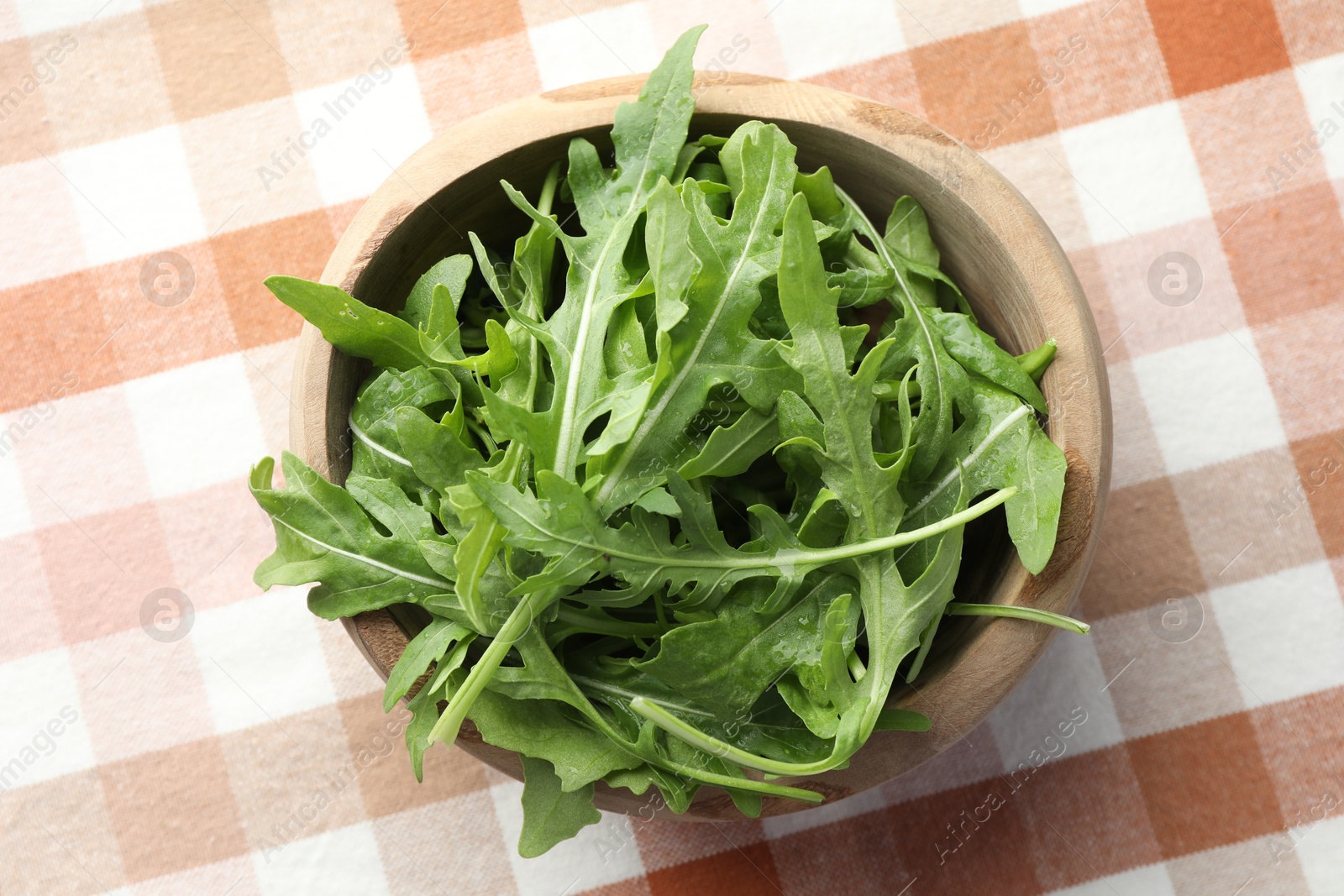 Photo of Fresh green arugula leaves in bowl on tablecloth, top view