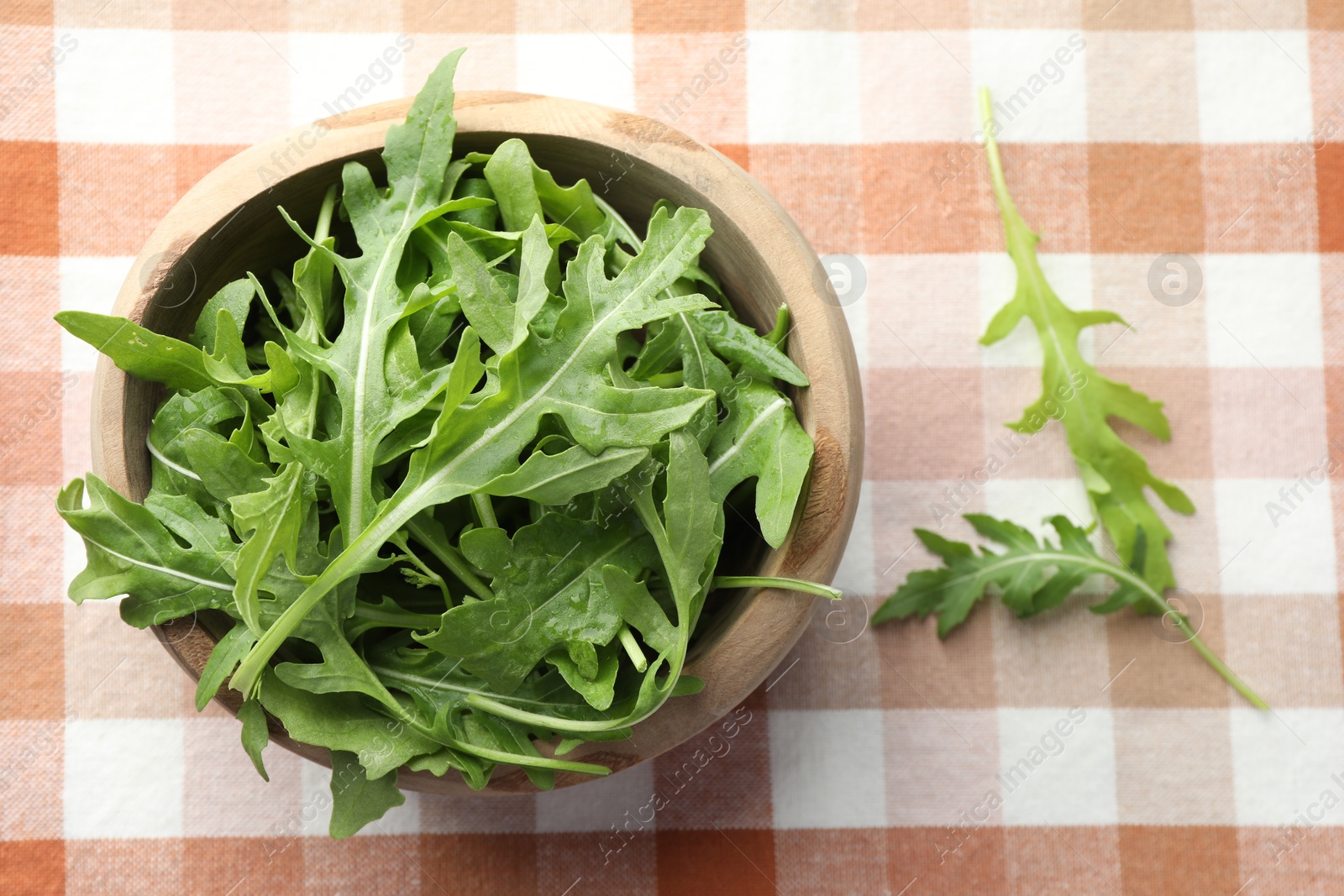 Photo of Fresh green arugula leaves in bowl on tablecloth, top view