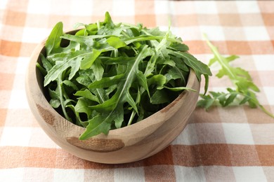 Photo of Fresh green arugula leaves in bowl on tablecloth, closeup