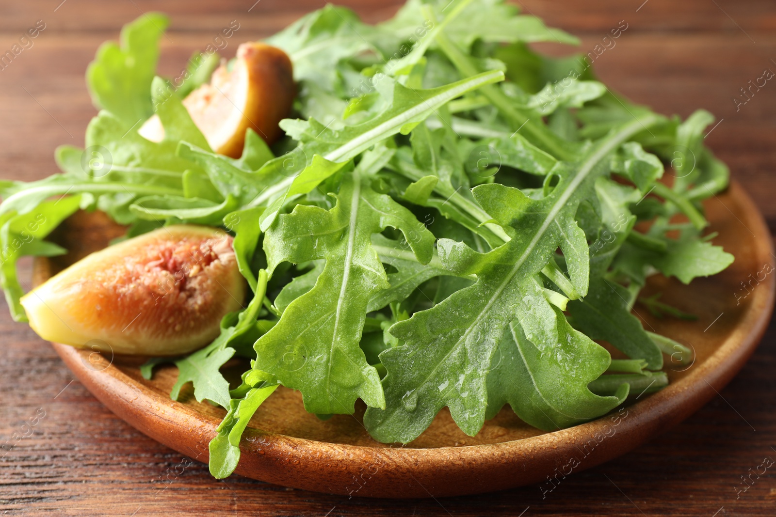 Photo of Fresh green arugula leaves and cut fig on wooden table, closeup