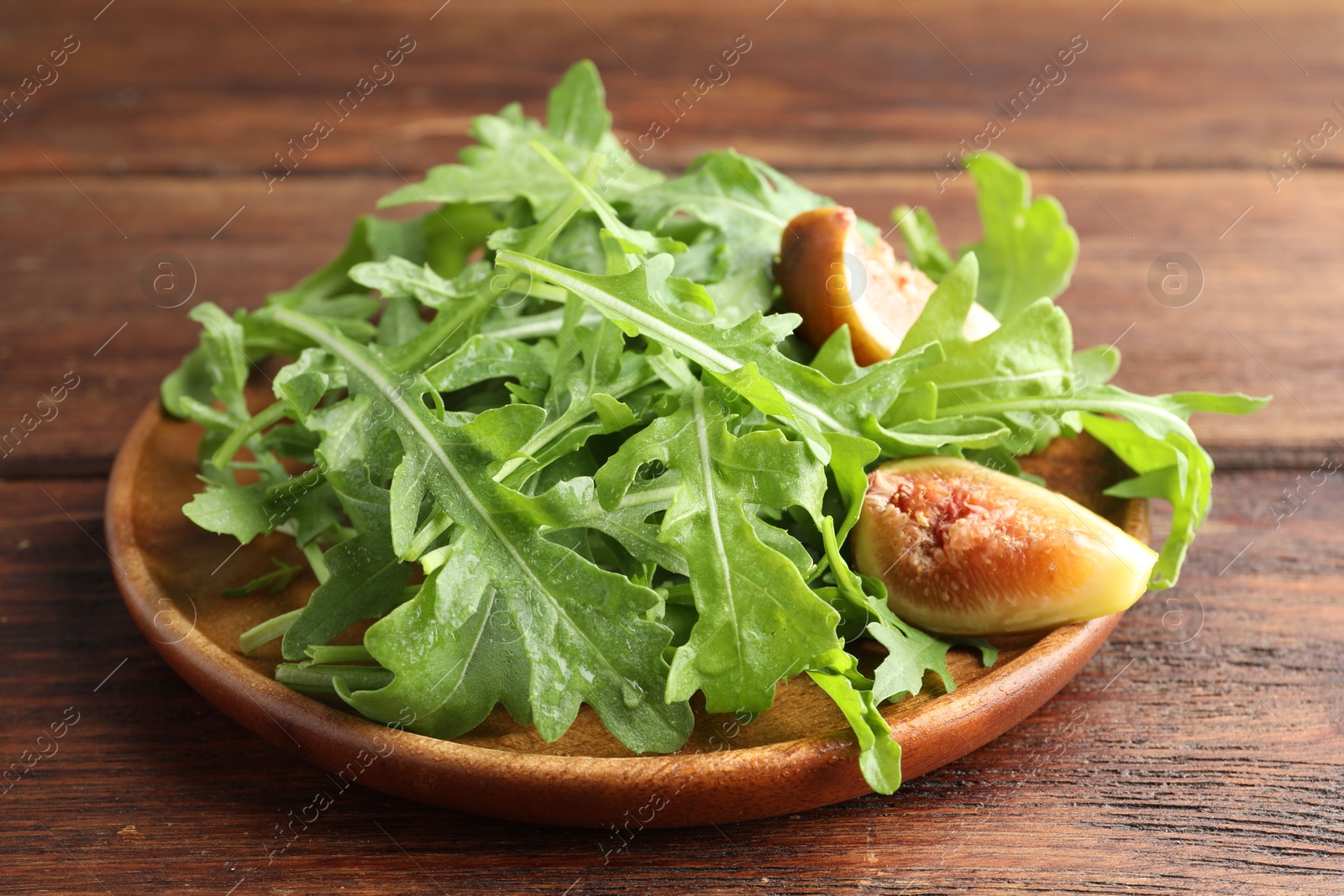 Photo of Fresh green arugula leaves and cut fig on wooden table, closeup