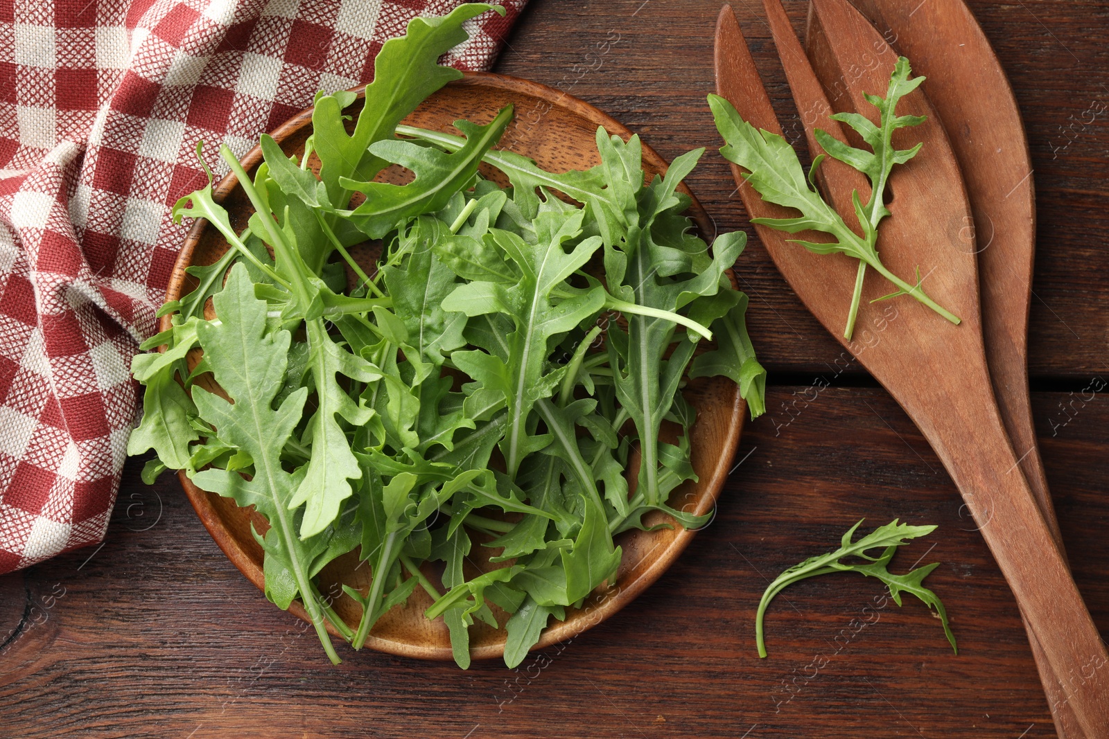 Photo of Fresh green arugula leaves and cutlery on wooden table, flat lay